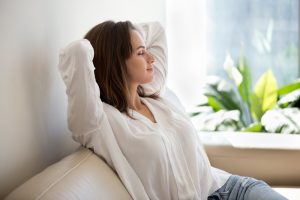 Woman in loose fitting clothing relaxes on the couch after her breast augmentation.