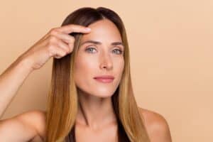 Brunette woman points to her forehead pleased with her rejuvenated brow