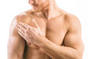 Muscular man rubs his sore shoulder after a sports injury