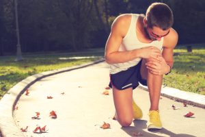 Jogging man clutches knee in pain.