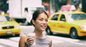 Chic woman drinks coffee as she walks on a NYC sidewalk near cabs.