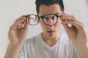 Man holds glasses away from his face - changing prescription could be a sign of keratoconus.