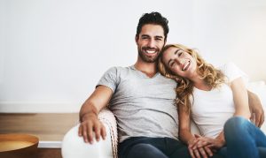Attractive couple sits on the couch. They cuddle and smile